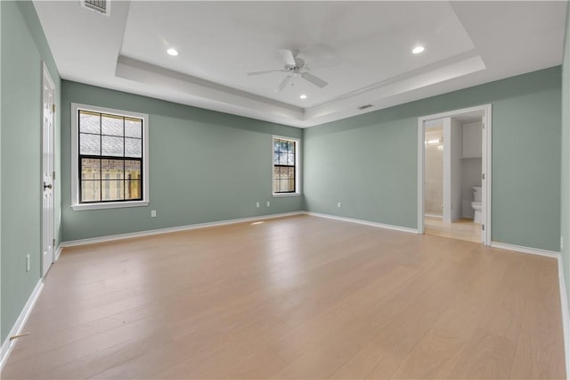 empty room with a healthy amount of sunlight, baseboards, light wood-type flooring, and a tray ceiling