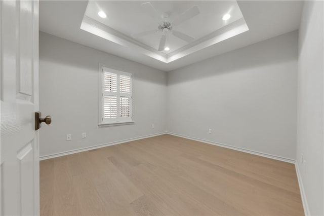 unfurnished room with baseboards, a raised ceiling, a ceiling fan, and wood finished floors