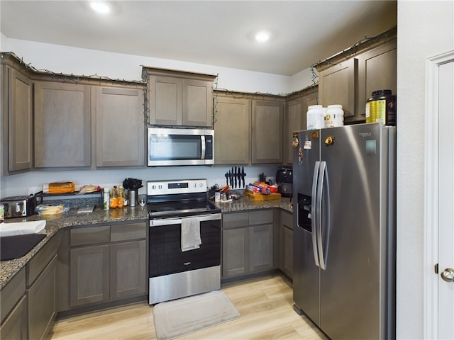 kitchen featuring appliances with stainless steel finishes, light hardwood / wood-style flooring, dark stone counters, and sink