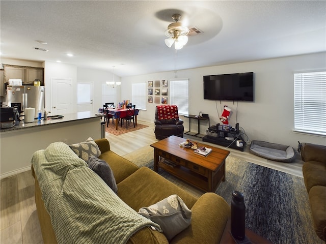 living room featuring a textured ceiling, ceiling fan with notable chandelier, and light hardwood / wood-style flooring