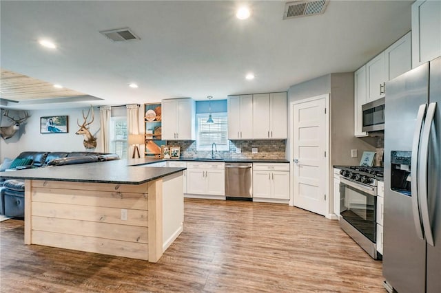 kitchen with a breakfast bar, appliances with stainless steel finishes, light hardwood / wood-style floors, decorative backsplash, and white cabinets