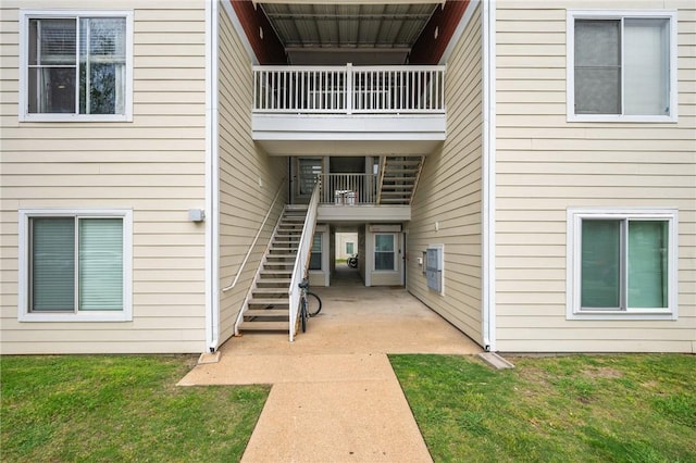 entrance to property with a patio area, a lawn, and a balcony