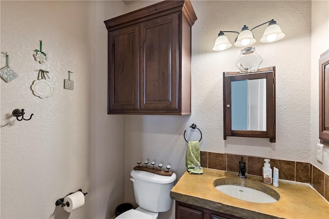 half bathroom with toilet, vanity, and a textured wall