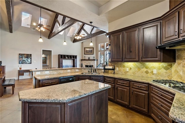 kitchen with a ceiling fan, vaulted ceiling with skylight, a sink, stainless steel gas stovetop, and backsplash