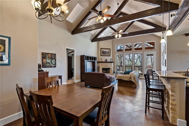 dining room featuring baseboards, high vaulted ceiling, a fireplace, dark tile patterned floors, and ceiling fan with notable chandelier