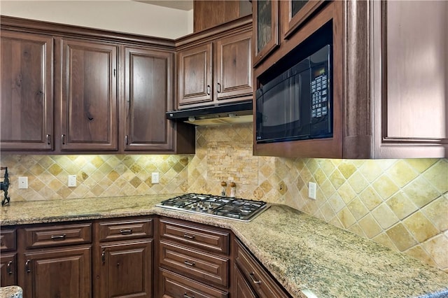 kitchen with under cabinet range hood, tasteful backsplash, black microwave, and stainless steel gas stovetop