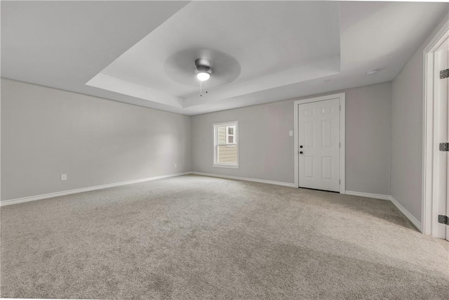 spare room featuring a raised ceiling, light carpet, and ceiling fan