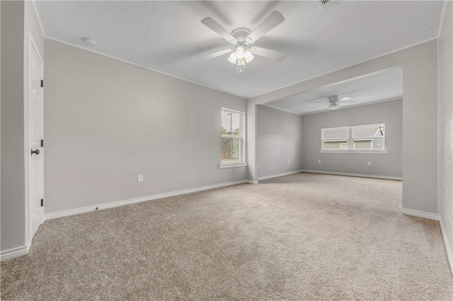 carpeted spare room featuring ceiling fan, ornamental molding, and plenty of natural light