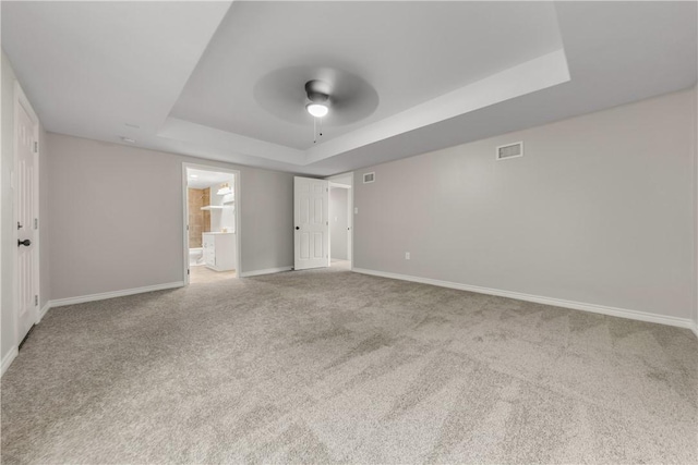 unfurnished bedroom with connected bathroom, a raised ceiling, ceiling fan, and carpet