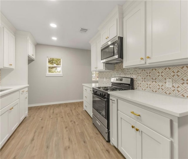 kitchen with appliances with stainless steel finishes, white cabinets, backsplash, and light hardwood / wood-style flooring