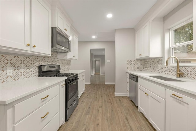 kitchen with appliances with stainless steel finishes, white cabinetry, sink, decorative backsplash, and light hardwood / wood-style flooring