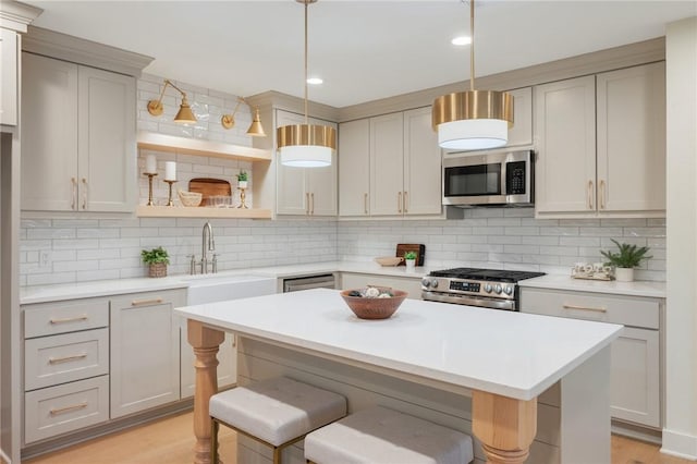 kitchen with decorative light fixtures, backsplash, gray cabinets, a kitchen breakfast bar, and stainless steel appliances