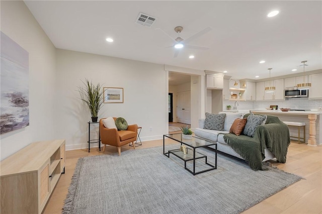 living room with ceiling fan, sink, and light hardwood / wood-style floors