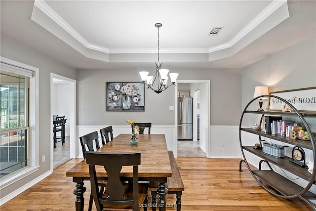 dining room featuring light hardwood / wood-style floors, a raised ceiling, crown molding, and an inviting chandelier