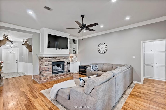 living room featuring hardwood / wood-style flooring, ceiling fan, ornamental molding, and a fireplace