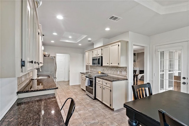 kitchen featuring stainless steel appliances, a raised ceiling, crown molding, dark stone counters, and decorative backsplash