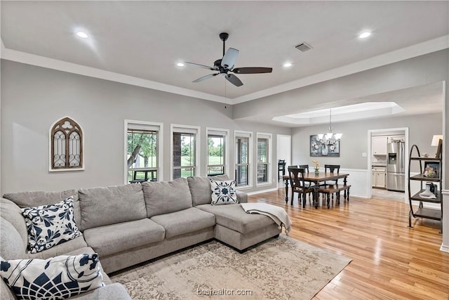 living room featuring a tray ceiling, crown molding, wood-type flooring, and ceiling fan with notable chandelier