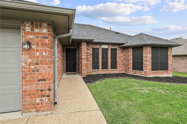 property entrance with roof with shingles, brick siding, and a yard