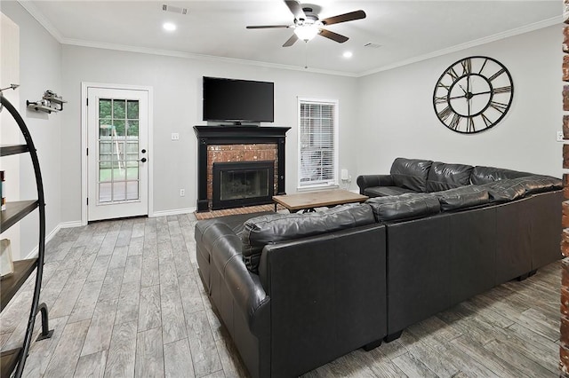 living area with wood finished floors, ceiling fan, a brick fireplace, crown molding, and baseboards