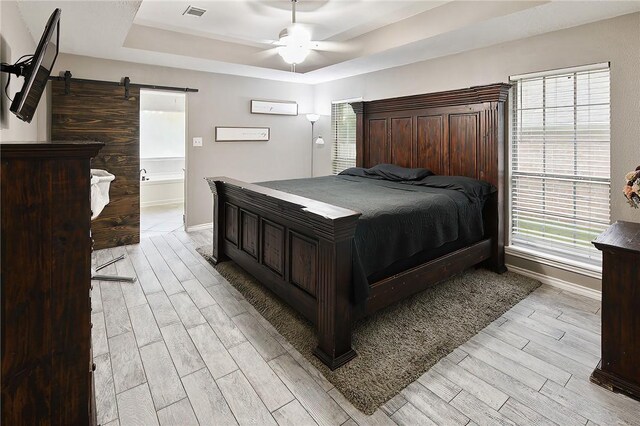 bedroom featuring a tray ceiling, a barn door, light wood-style flooring, baseboards, and a ceiling fan