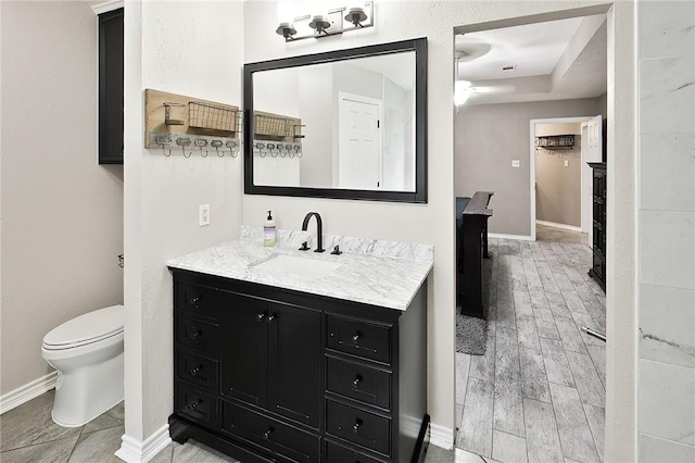 bathroom featuring toilet, baseboards, vanity, and a tray ceiling