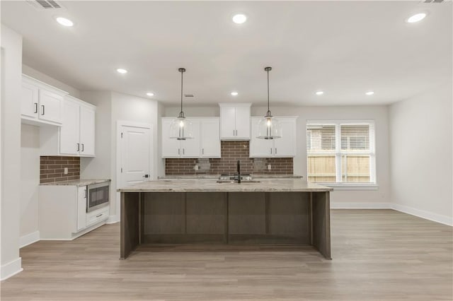 kitchen with hanging light fixtures, a center island with sink, white cabinets, and stainless steel microwave