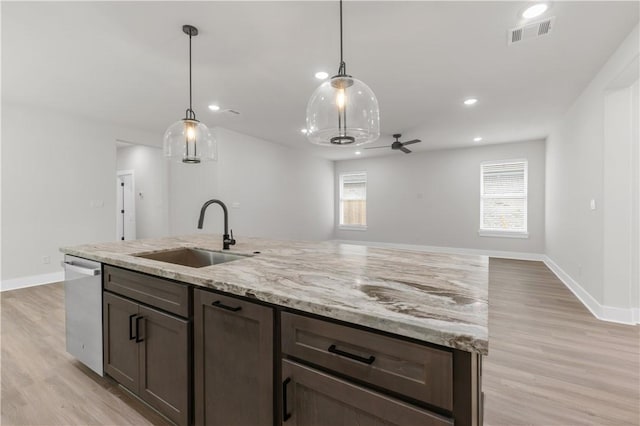 kitchen featuring pendant lighting, sink, a kitchen island with sink, stainless steel dishwasher, and light stone countertops