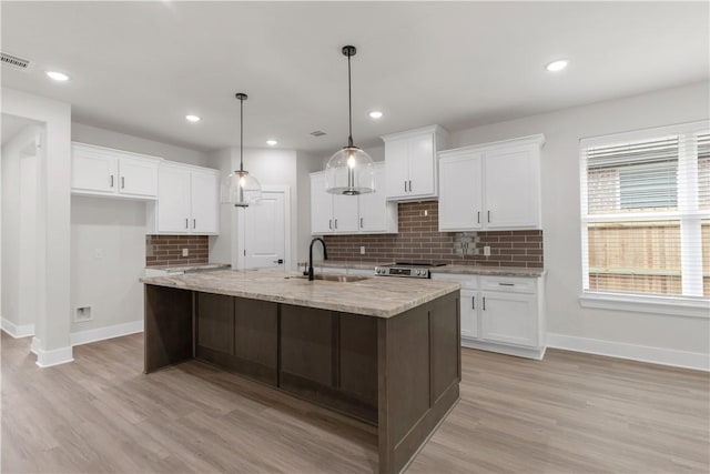 kitchen featuring sink, a center island with sink, white cabinets, and decorative light fixtures