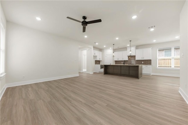 kitchen featuring white cabinetry, light hardwood / wood-style flooring, an island with sink, pendant lighting, and decorative backsplash