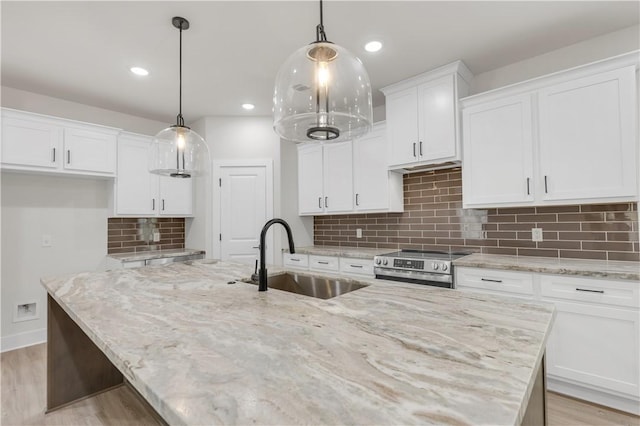 kitchen with decorative light fixtures, sink, a center island with sink, and white cabinets