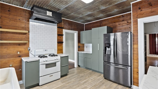 kitchen with stainless steel refrigerator with ice dispenser, white gas range, wood walls, light countertops, and light wood finished floors