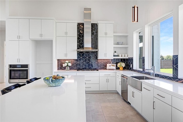 kitchen with decorative light fixtures, white cabinetry, wall chimney exhaust hood, light tile patterned flooring, and appliances with stainless steel finishes