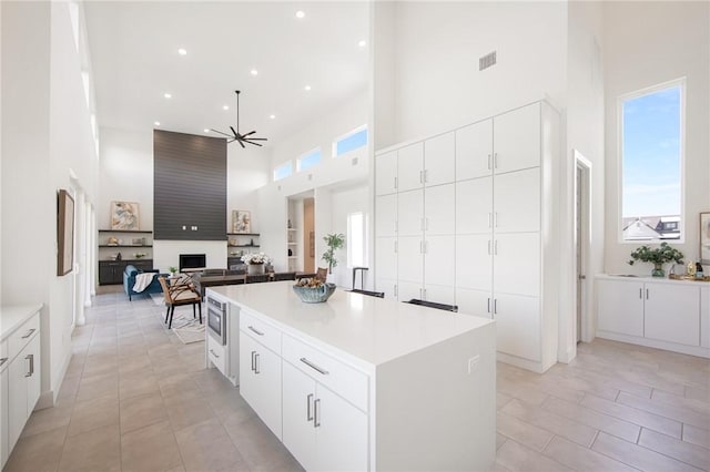 kitchen featuring white cabinets, ceiling fan, a kitchen island, stainless steel microwave, and a high ceiling