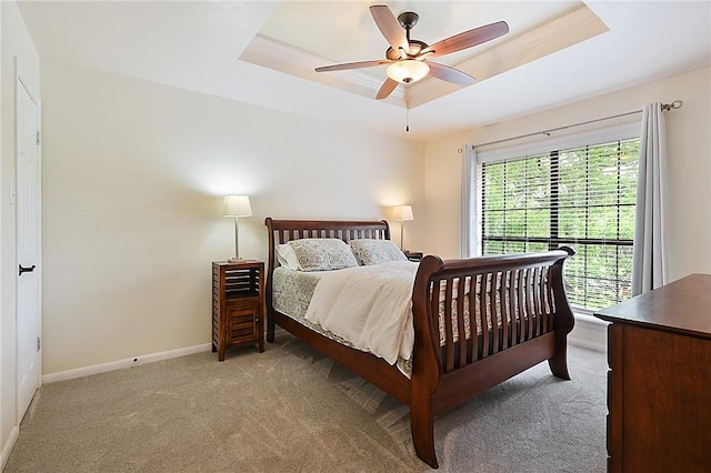 carpeted bedroom with a raised ceiling and ceiling fan