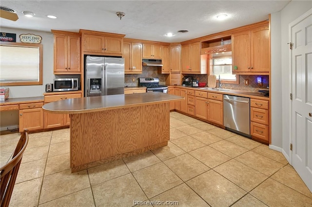 kitchen with a center island, backsplash, sink, light tile patterned floors, and appliances with stainless steel finishes