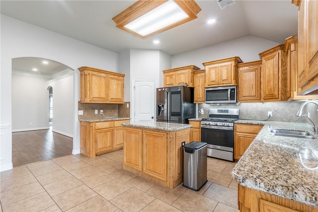 kitchen with lofted ceiling, sink, appliances with stainless steel finishes, a kitchen island, and light stone countertops