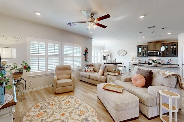 living room with light wood-type flooring and ceiling fan with notable chandelier