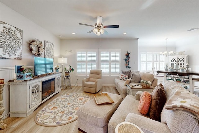 living room with light wood-type flooring and ceiling fan with notable chandelier