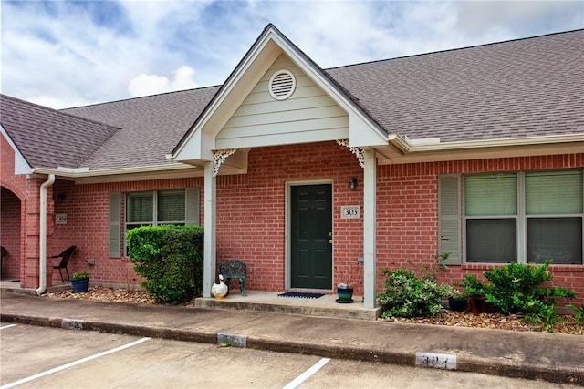 entrance to property featuring brick siding and a shingled roof