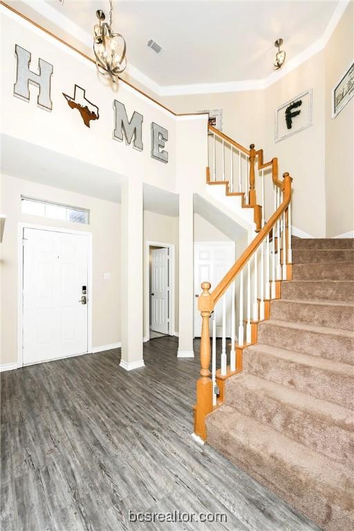 foyer with a high ceiling, dark hardwood / wood-style flooring, an inviting chandelier, and crown molding