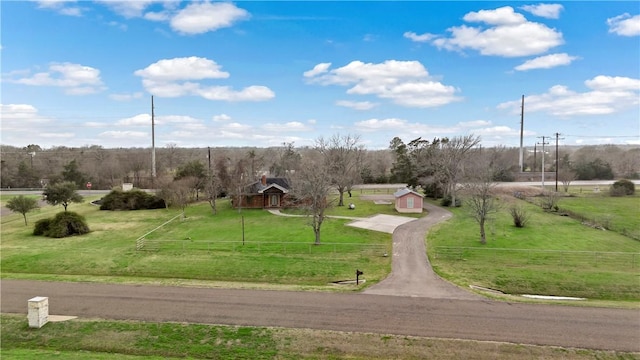 view of community with fence, a lawn, and a rural view