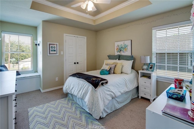 bedroom featuring a tray ceiling, crown molding, a closet, a ceiling fan, and light carpet