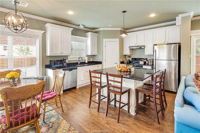 kitchen featuring stainless steel appliances, dark countertops, white cabinetry, a sink, and a kitchen island