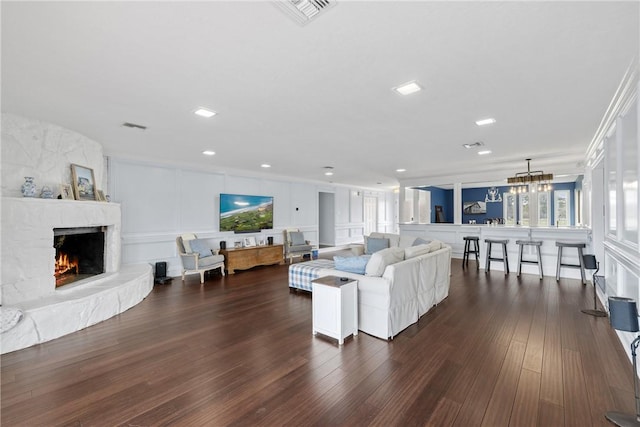 living area with visible vents, dark wood finished floors, a stone fireplace, a decorative wall, and a chandelier