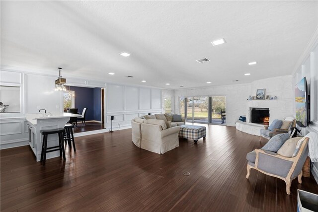 living area featuring dark wood finished floors, visible vents, a decorative wall, and a lit fireplace