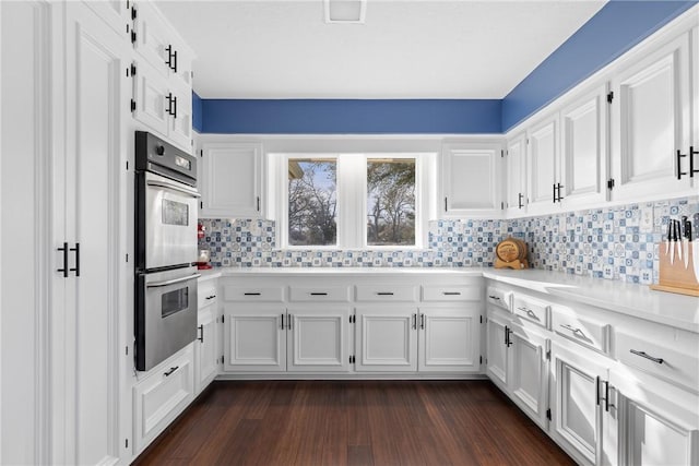 kitchen featuring double oven, light countertops, decorative backsplash, white cabinets, and dark wood-style flooring