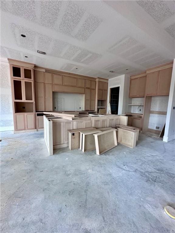 kitchen with a center island, light brown cabinets, a textured ceiling, and unfinished concrete floors