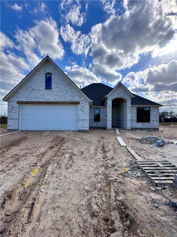 view of front of house featuring dirt driveway, brick siding, and a garage