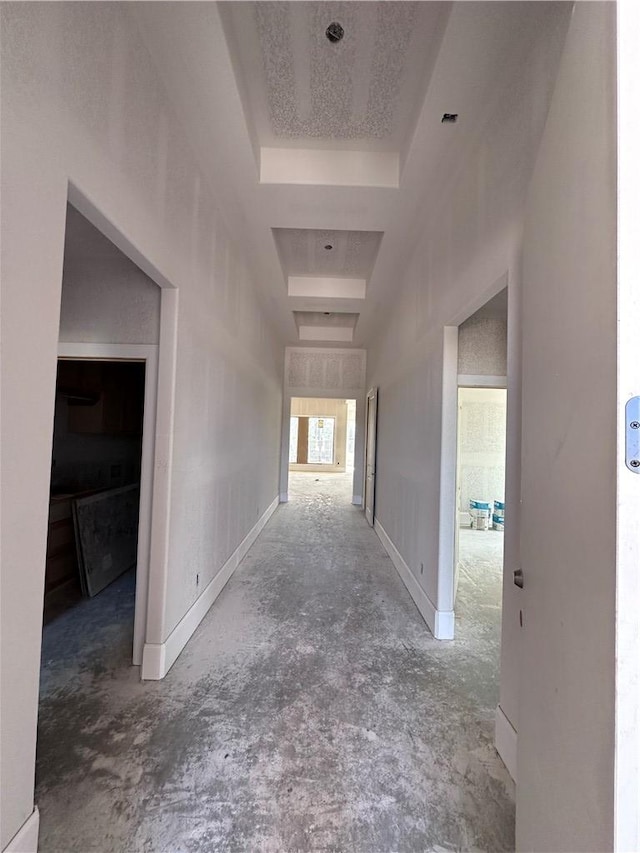 hallway with a textured ceiling, a tray ceiling, a high ceiling, and baseboards