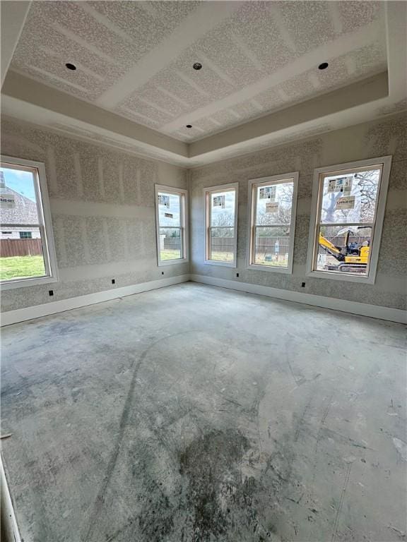 empty room with a tray ceiling, a wealth of natural light, and baseboards